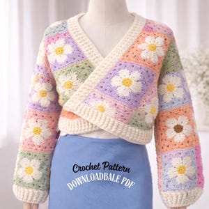 May include: A colorful, crocheted wrap sweater featuring daisy flower motifs. The sweater is made of squares in pastel colors, including pink, purple, green, and peach. The text "Crochet Pattern DOWNLOADABLE PDF" is visible on the bottom.
