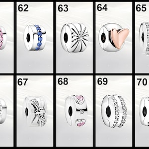 Op de afbeelding: Een verzameling zilverkleurige bedel kralen met diverse ontwerpen. Sommige kralen hebben roze of blauwe edelstenen, terwijl andere hart-, ster-, strik- of bloempatronen hebben. Elke kraal heeft een centraal gat om te rijgen.