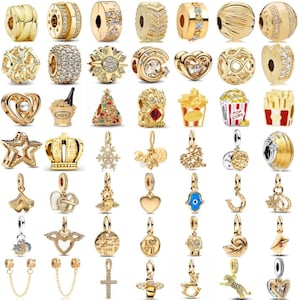 May include: A selection of gold-coloured charm beads and pendants. Designs include hearts, stars, crowns, and other decorative elements. Some charms are embellished with clear crystals and gemstones.