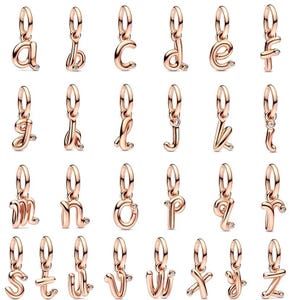 May include: A collection of rose gold-colored alphabet charms, each featuring a cursive letter design and a small, clear gemstone. The charms are suspended from a loop, ready to be added to a bracelet or necklace.