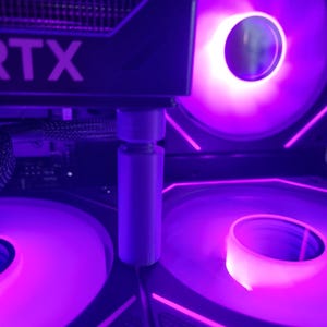 Könnte beinhalten: Nahaufnahme der internen Komponenten eines Computers, beleuchtet mit violetten LED-Leuchten. Das Bild zeigt eine Grafikkarte mit "RTX"-Branding und mehrere Lüfter. Die Lüfter sind mit einem hellen violetten Schein beleuchtet.