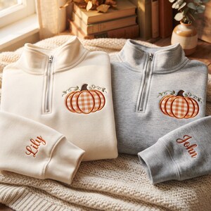 May include: Two quarter-zip sweatshirts, one cream and one heather gray, each featuring an embroidered orange and white gingham pumpkin on the chest. The cream sleeve is embroidered with the name Lily, and the gray sleeve with the name John.