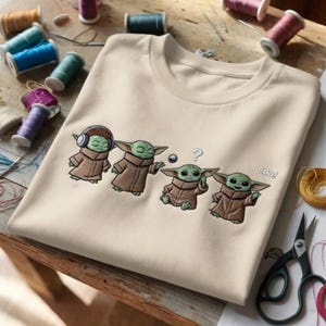 Puede incluir: Sudadera beige de cuello redondo con un dise&ntilde;o bordado de Grogu de The Mandalorian. El dise&ntilde;o muestra a Grogu en cuatro poses diferentes, con la palabra "coo!" al lado de una. Suministros de costura en el fondo.