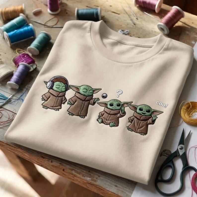 Puede incluir: Sudadera beige de cuello redondo con un dise&ntilde;o bordado de Grogu de The Mandalorian. El dise&ntilde;o muestra a Grogu en cuatro poses diferentes, con la palabra "coo!" al lado de una. Suministros de costura en el fondo.