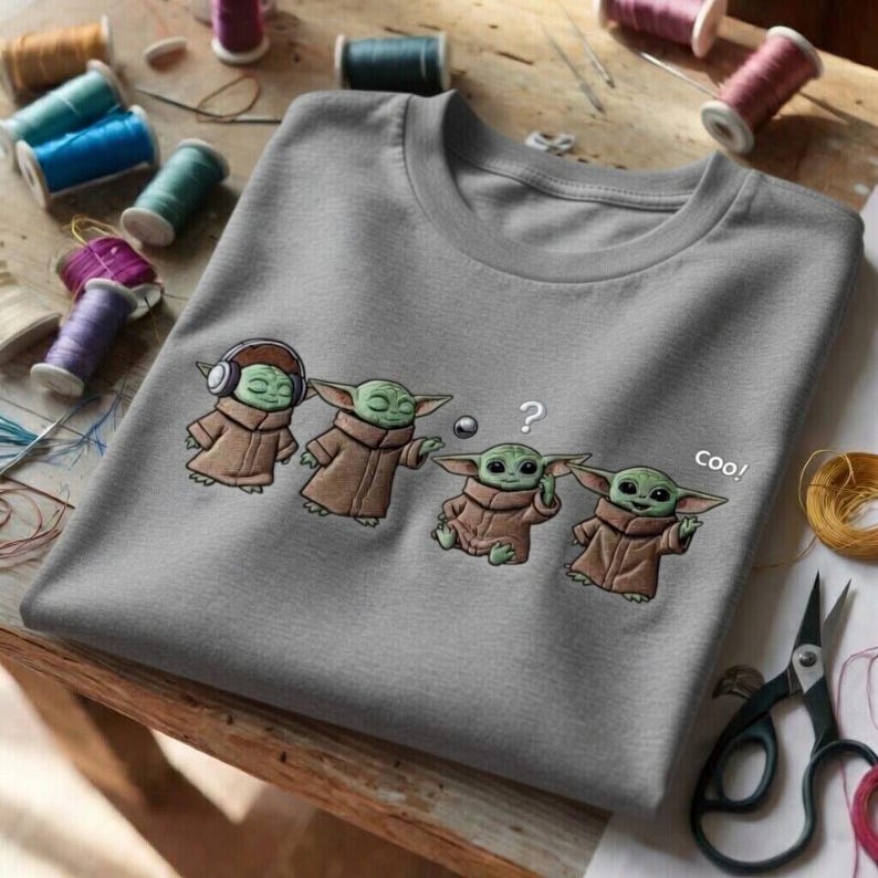 Puede incluir: Una camiseta gris de cuello redondo con un dise&ntilde;o bordado de cuatro personajes de Grogu. Un Grogu lleva auriculares, otro tiene un signo de interrogaci&oacute;n y el &uacute;ltimo dice "coo!"