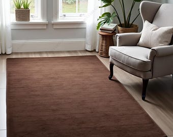May include: A rectangular brown rug with a soft texture, placed on a light-coloured wooden floor. The rug is the focal point of a room, with a neutral colour palette. The room includes a chair, plants, and a window.