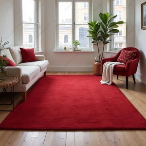 May include: A vibrant red rectangular rug fills the floor space of a living room. A white sofa with red cushions is on the left, and a red armchair with a patterned cushion and a blanket is on the right. The rug is placed on a light-colored wooden floor.