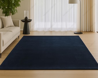 May include: A large, rectangular navy blue rug dominates the foreground. The rug is placed on a light-colored hardwood floor. The room also features a beige sofa, a black side table, and a floor lamp with a white lampshade.