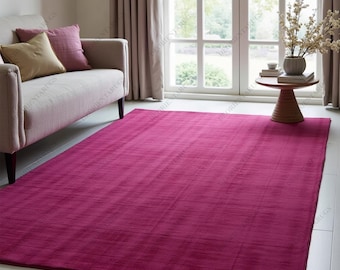 May include: A large, rectangular magenta rug with a subtle striped texture. The rug is placed on a white tiled floor in a living room setting, with a sofa and window in the background. The rug's dimensions are not visible.