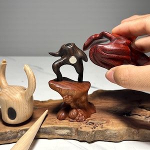 Peut inclure: Sculptures en bois de diff&eacute;rentes formes et couleurs. L'une est une pi&egrave;ce claire en forme de corne avec un ovale noir. Une autre est une figure abstraite brun fonc&eacute; sur une base en bois. Une troisi&egrave;me est une forme organique rouge fonc&eacute;.