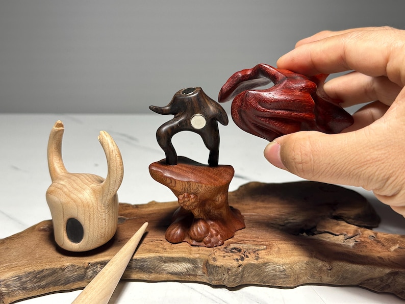 Peut inclure: Sculptures en bois de diff&eacute;rentes formes et couleurs. L'une est une pi&egrave;ce claire en forme de corne avec un ovale noir. Une autre est une figure abstraite brun fonc&eacute; sur une base en bois. Une troisi&egrave;me est une forme organique rouge fonc&eacute;.