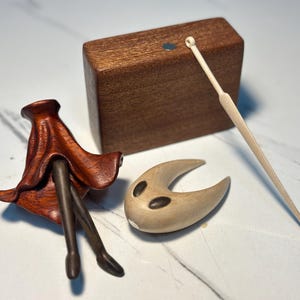 May include: A selection of wooden figurines. Features a dark brown, flower-like sculpture, a light brown crescent-shaped piece with dark markings, a rectangular block, and a thin, light-coloured stick.