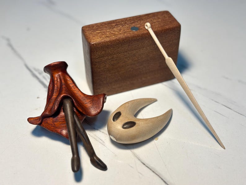 May include: A selection of wooden figurines. Features a dark brown, flower-like sculpture, a light brown crescent-shaped piece with dark markings, a rectangular block, and a thin, light-coloured stick.
