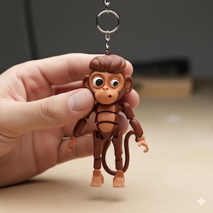 May include: A brown articulated monkey keychain with a surprised expression. The keychain has a silver ring and chain. The monkey has large eyes, a small mouth, and a curly tail. The monkey is made of plastic.