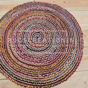 Puede incluir: Una alfombra redonda de yute con un diseño en espiral. La alfombra presenta una mezcla de colores como amarillo, azul, rojo y verde. La alfombra está colocada sobre un suelo de madera.