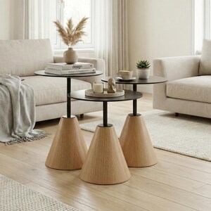 Op de afbeelding: Drie moderne bijzettafels met zwarte bladen en conische houten bases. De tafels staan in een woonkamer met beige banken, een vloerkleed en natuurlijk licht. Decoratieve items worden op de tafels getoond.