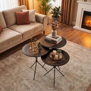 Può includere: Un set di tre tavolini rotondi neri con un esclusivo design a venature del legno. Ogni tavolo ha una base a treppiede ed è disposto in gruppo. I tavoli sono in un soggiorno con un divano e un tappeto beige.