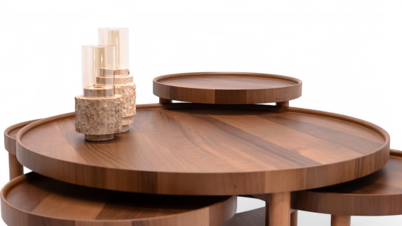 May include: A set of contemporary, circular wooden coffee tables in different sizes. The tables are crafted from dark brown wood with a smooth, polished finish. Two glass candle holders with a textured base are placed on the largest table.