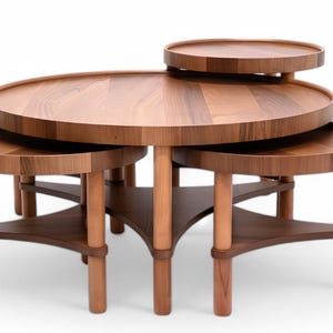 May include: A set of four wooden nesting tables with a natural finish. The tables have round tops and are supported by cylindrical legs and triangular supports. The largest table is approximately 91 cm in diameter.