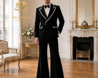 May include: A black double-breasted suit featuring a blazer with silver stud embellishments along the lapels and pockets, paired with wide-leg trousers. The ensemble includes a white dress shirt and a black bow tie. The logo SUIT SYNC is visible.