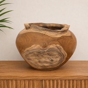 Peut inclure: Un bol en bois arrondi fabriqué en teck naturel, doté d'une large ouverture irrégulière et d'une surface lisse et polie qui met en valeur les motifs de grain complexes et tourbillonnants ainsi que les tons brun profond du bois.