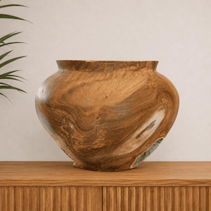 Può includere: Un grande recipiente in legno arrotondato ricavato da un unico pezzo di legno marrone chiaro. L'oggetto presenta un corpo ampio e bulboso con un'apertura stretta sulla parte superiore, che mette in mostra venature naturali, vortici e texture.