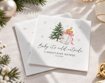 May include: Two white square paper napkins featuring a watercolor illustration of a green pine tree, a baby bottle with a pink ribbon, and snowflakes. The text reads: Baby it's cold outside, CAMILE'S BABY SHOWER, and the date 12.21.2026.