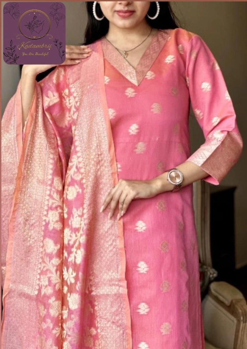 May include: Pink Indian kurta suit with a matching dupatta. The kurta features a V-neck and floral pattern. The dupatta has a gold floral design. The outfit is made of a lightweight fabric.