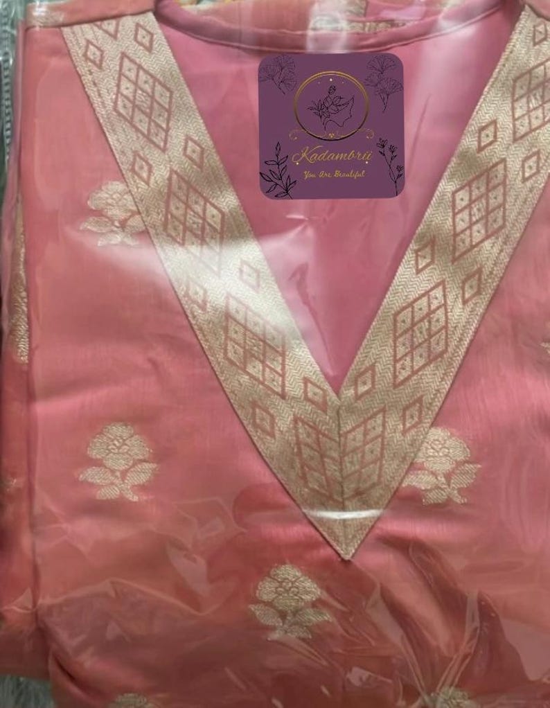 May include: A pink garment with a V-neck design, featuring gold floral patterns and a decorative gold border. The garment has a tag with the text "Kadambrii You Are Beautiful".