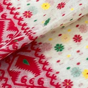 May include: White fabric with a red patterned border and scattered floral designs in red, green, and yellow. The fabric has a delicate, semi-transparent appearance, suggesting a lightweight material like cotton or silk. The design is likely for a scarf or shawl.