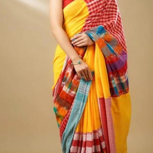 May include: A vibrant yellow saree with a red and white checkered border and a multicolored patterned pallu. The saree is draped over a red top. The image features a woman wearing the saree.