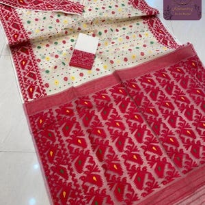 Puede incluir: Un textil color crema con un diseño estampado en rojo y blanco. La tela presenta un patrón geométrico repetitivo en rojo, con detalles en amarillo y verde. También se ve una pieza más pequeña y a juego.