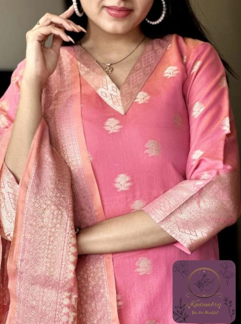 May include: Pink Indian kurta suit with gold floral patterns. The suit features a V-neckline and three-quarter sleeves. The dupatta and sleeve cuffs have a gold geometric design. The suit has the text "Kadambrii You are Beautiful" in the bottom right corner.