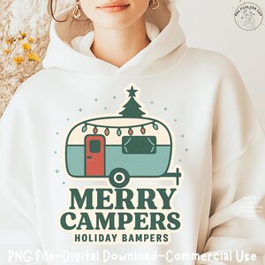 May include: White hooded sweatshirt with a teal and red campervan design, topped with a Christmas tree. The text "MERRY CAMPERS HOLIDAY BAMPERS" is below. The design includes string lights and star accents.