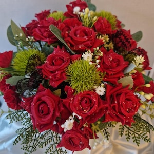 May include: A floral arrangement featuring deep red roses, bright green spiky thistle-like accents, small white filler flowers, and green foliage. Two black butterfly ornaments are nestled among the flowers, which are accented with water droplets.