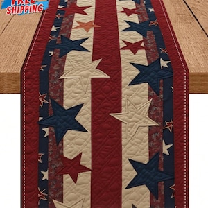 May include: Quilted table runner with a patriotic theme. The runner features a pattern of red and cream stripes with blue, red, and cream stars. The runner is made of a quilted fabric and has a rectangular shape.
