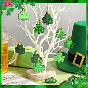 May include: A festive St. Patrick's Day display with green shamrock ornaments suspended from a white tree. A green leprechaun hat and a gift box are also present. The ornaments have gold caps and are hung by gold strings.