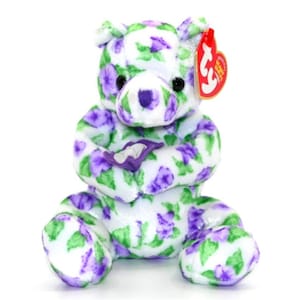 May include: A plush bear toy with a white base, covered in a pattern of purple flowers and green leaves. The bear has black eyes, a purple nose, and a red tag attached to its ear.