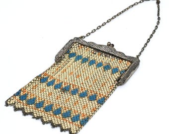 May include: An antique silver mesh purse with a chain handle. The purse features a decorative frame and a patterned mesh design in cream, orange, and blue. The purse is likely from the early 20th century.