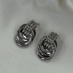 May include: A pair of silver-toned earrings. Each earring features a design of intertwined, rounded metal loops. The earrings have a post backing for secure wear. The jewelry is displayed on a white surface.