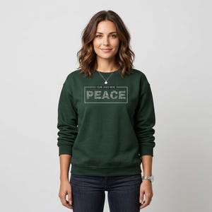 May include: A dark green sweatshirt with the text "PEACE" in a rectangular frame. Above the word "PEACE" is the text "FEAR LOSES HERE". The sweatshirt is a solid color and has long sleeves.