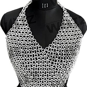 May include: A silver-colored chainmail halter top displayed on a black mannequin. The top features a V-neck design and a matching chain that wraps around the waist. The metal links are intricately woven, creating a mesh-like pattern.
