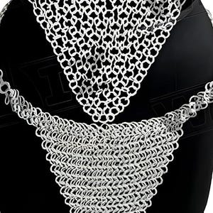 May include: A silver chainmail garment, likely a neck piece, displayed against a black background. The chainmail is made of small, interlocking metal rings, creating a flexible, textured surface. The design includes a triangular section and a longer, draped section.