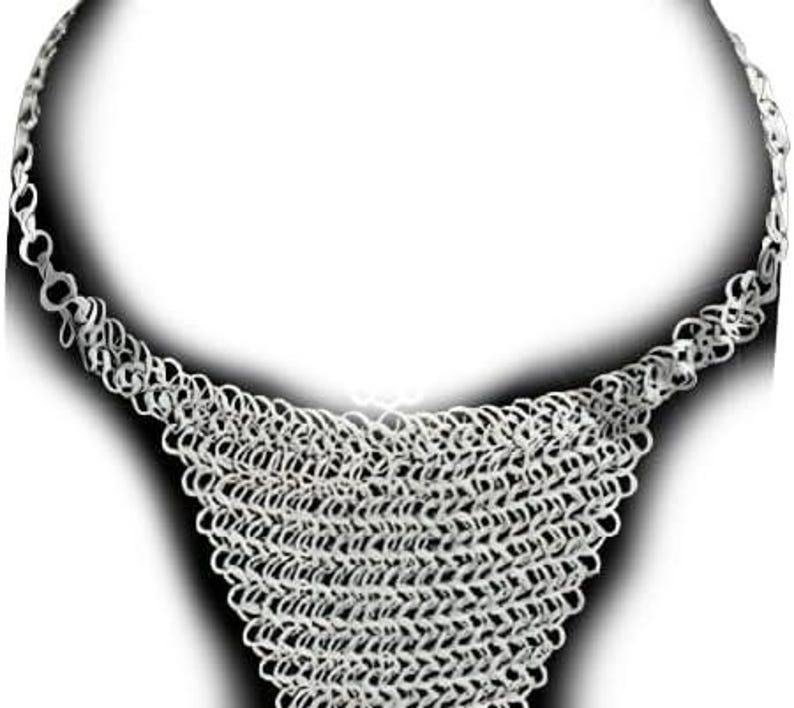 May include: A silver-colored chainmail necklace. The necklace features a wide, woven bib design that tapers to a chain. The chainmail is made of small, interlocking rings, creating a textured, metallic appearance. The necklace is displayed against a white background.