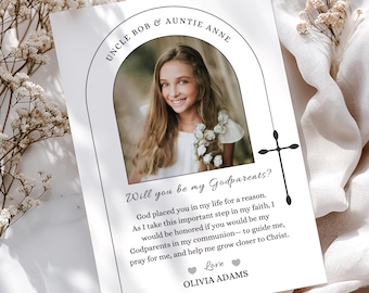 May include: A white card with a photo of a girl, text that reads "Uncle Bob & Auntie Anne" and "Will you be my Godparents?" The card includes a cross graphic and the name "Olivia Adams". The card is surrounded by white flowers.