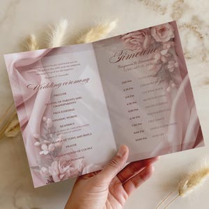 May include: A wedding program with a pink and white floral design. The program includes the wedding ceremony details and timeline for Benjamin & Samantha's February 10, 2026 wedding. The program is held in a hand.