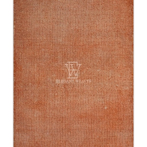 May include: A rectangular, rust-colored rug with a textured surface. The rug has a white fringe along the bottom edge. The words "ELEGANT WEAVES" are printed in white on the rug.