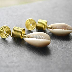 May include: A pair of gold wire wrapped earrings with a white cowrie shell on each end. The wire is wrapped in a spiral design.