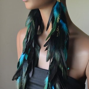 May include: Long black and teal feather earrings with gold accents. The earrings are dangling from the ears of a mannequin.