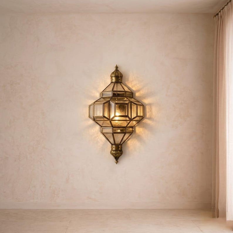 May include: A decorative wall-mounted lantern with a geometric design. The lantern is made of brass-colored metal and glass panels. It has a warm, inviting glow, casting light onto the surrounding wall. The lantern is a stylish home decor item.